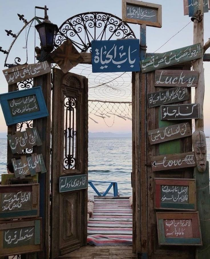 an open wooden door leading to the ocean with arabic writing on it and hanging signs