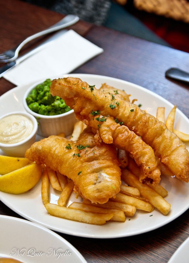 fish and chips on a white plate with lemon wedges next to the side dish