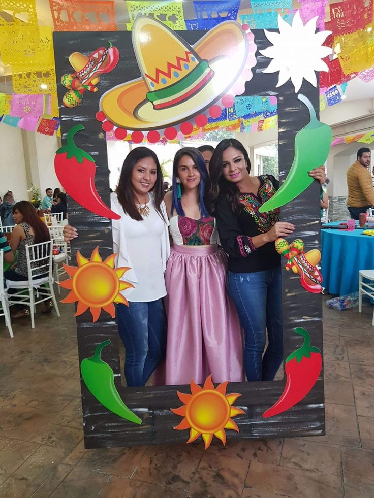 three women standing in front of a photo booth at a mexican themed party with decorations hanging from the ceiling