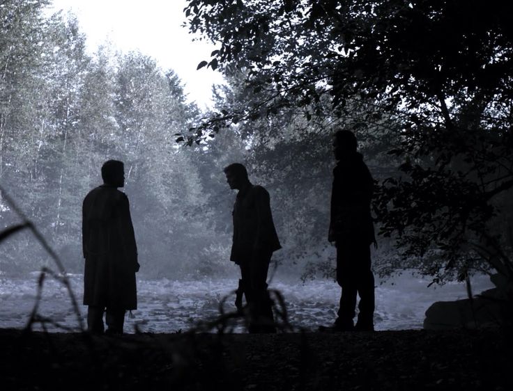 three people are standing in the dark near some trees