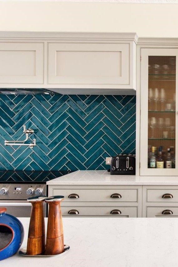 a kitchen with white cabinets and blue backsplash tiles on the countertop, along with copper accents