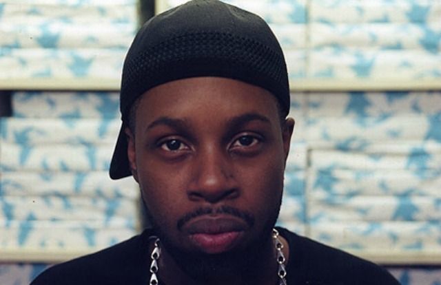 a man wearing a black hat and chain around his neck is staring at the camera