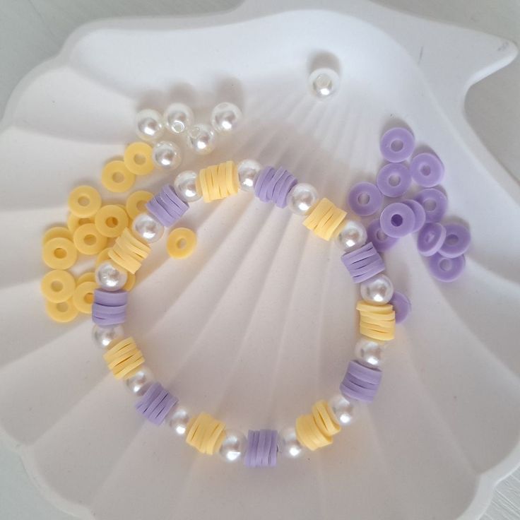 two bracelets with yellow and purple beads are sitting on a white platter,