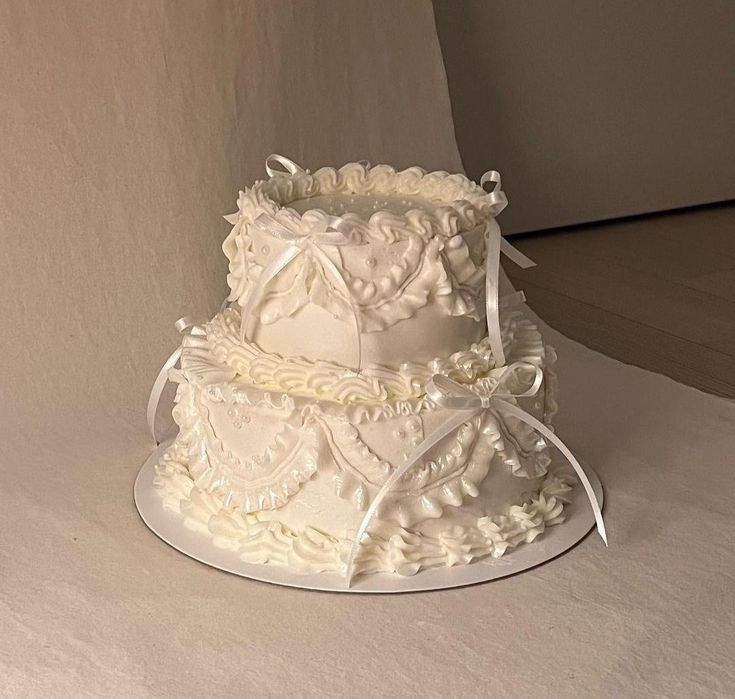 a three tiered wedding cake with white frosting and ribbon on top, sitting on a table