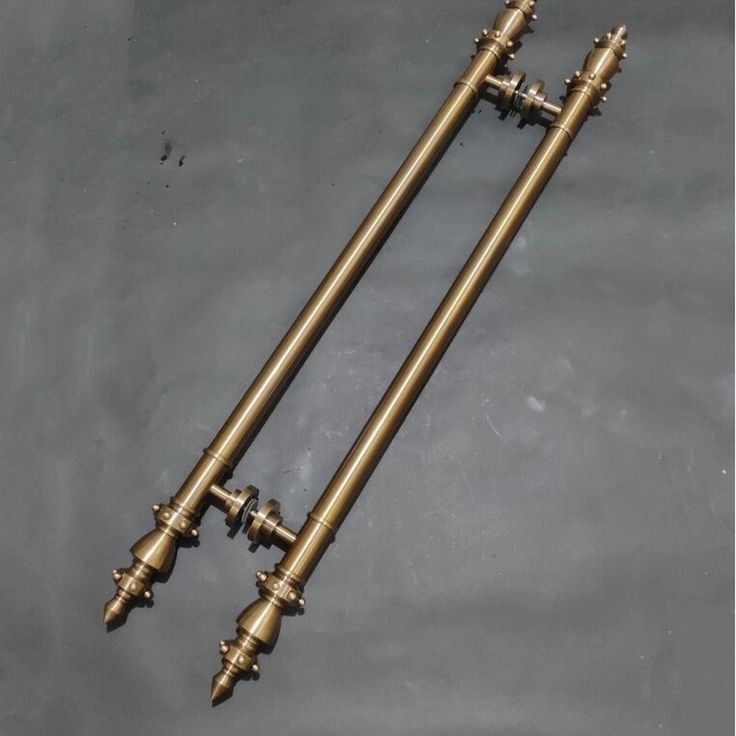 two antique brass candlesticks sitting side by side on a gray surface with one candle in the middle