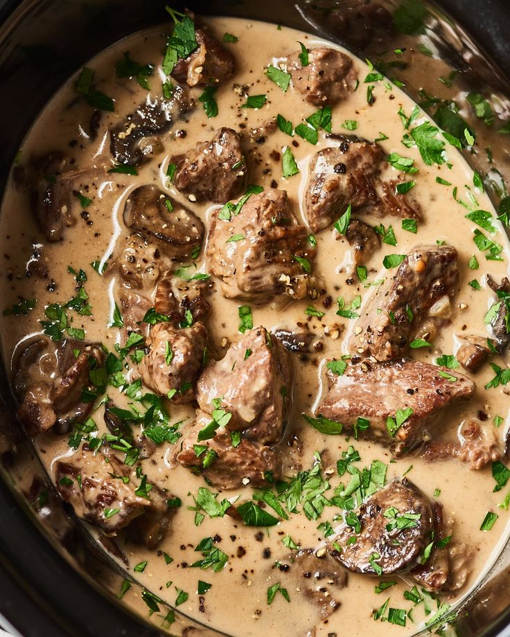 a crock pot filled with meat, mushrooms and gravy in cream sauce