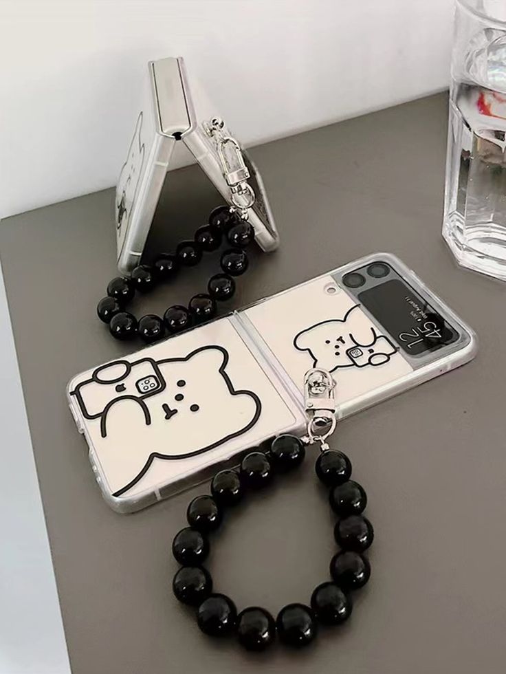 a cell phone with a black beaded necklace on it and a white cat case