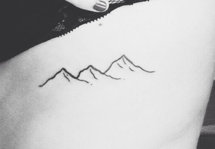 a black and white photo of a woman's stomach with mountains tattooed on it