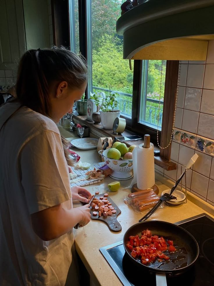 a woman cooking food in a kitchen next to a window