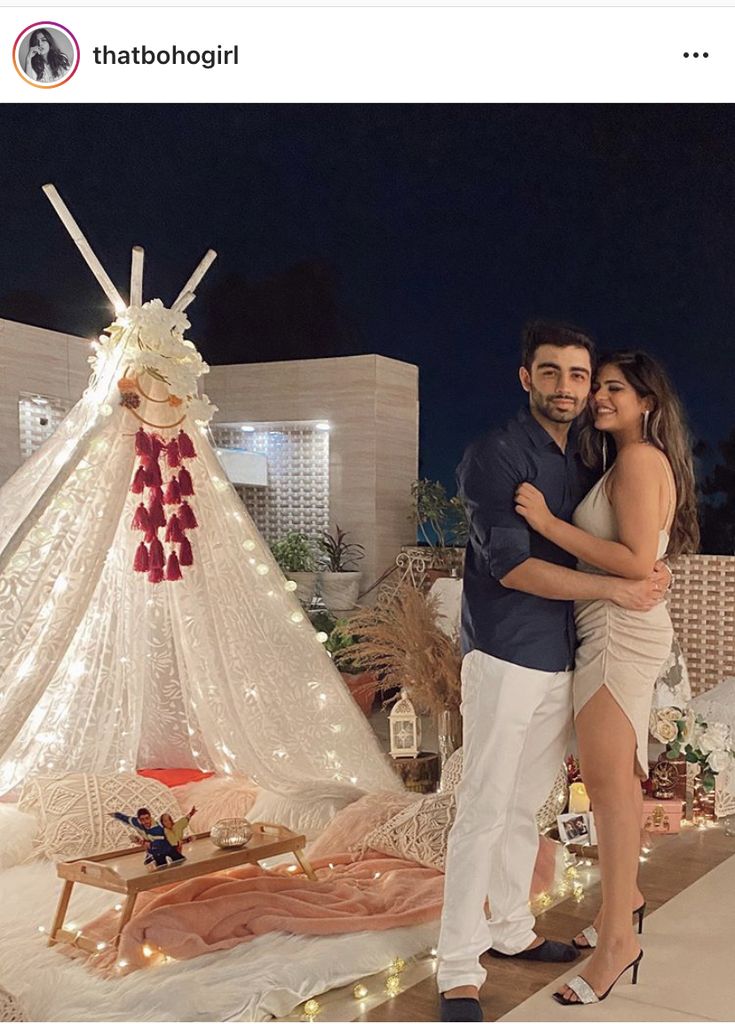 a man and woman standing in front of a teepee tent with lights on it