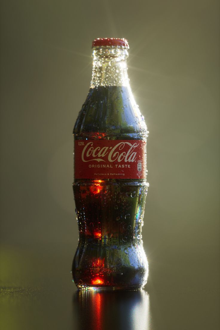 a bottle of coca - cola sitting on top of a table with the sun shining through it