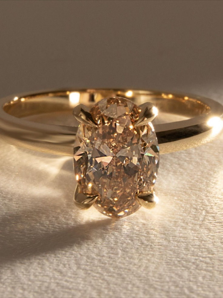 an oval shaped diamond sits on top of a gold band and is surrounded by two smaller round diamonds