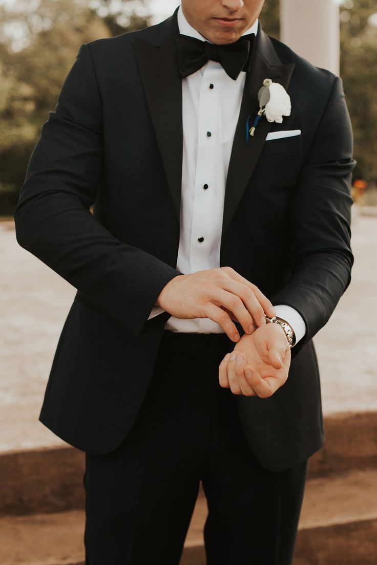 a man in a tuxedo adjusting his watch