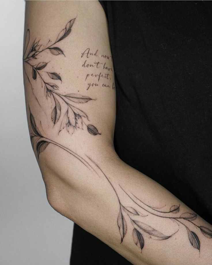 a woman's arm with some writing on it and leaves around the arm area