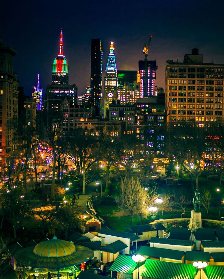 the city skyline is lit up at night with brightly colored lights on buildings and umbrellas