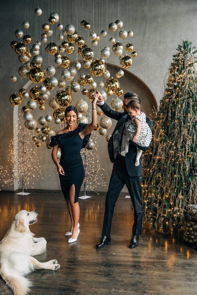 a man and woman dancing with a dog in front of a christmas tree decorated with ornaments