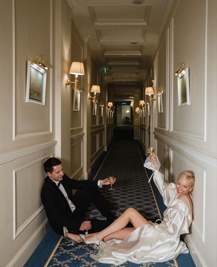 a man and woman are sitting on the floor in an elegant hotel hallway, drinking champagne