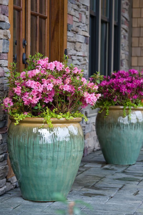 two large green vases filled with pink flowers on a stone walkway next to a brick building