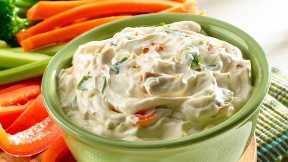 a green bowl filled with dip surrounded by carrots and broccoli