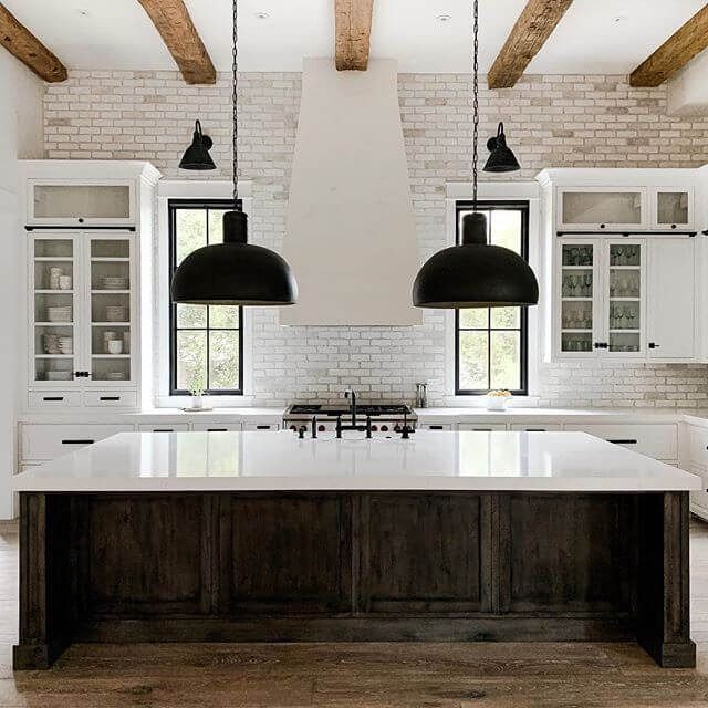 a kitchen with two black pendant lights hanging from the ceiling and an island in front of it