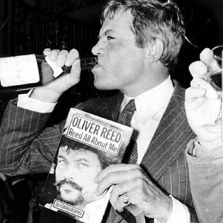 a man in a suit drinking from a bottle while holding up a paper with an image of himself on it