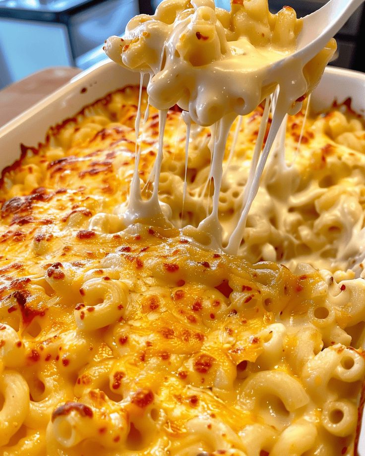 a spoon full of macaroni and cheese being lifted from a casserole dish