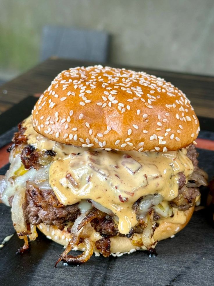 a cheeseburger with meat, onions and sauce on a black plate next to some fries