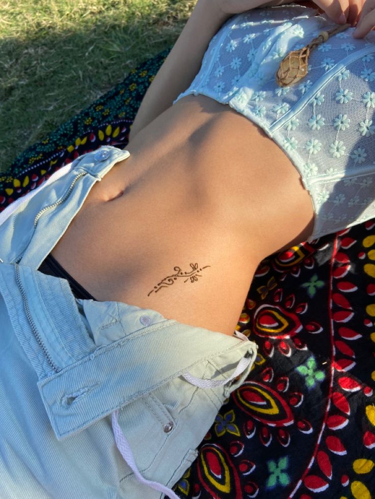 a woman laying on the ground with her back turned to the camera and tattoos on her stomach