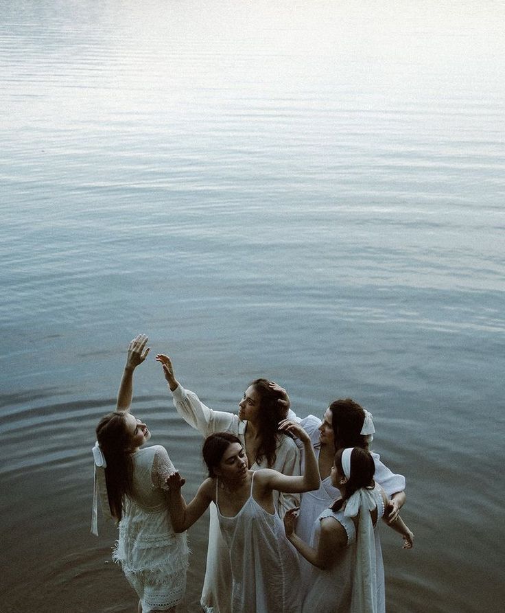 four women are standing in the water and one is holding her hand up to catch something