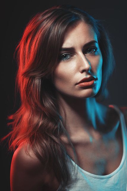 a woman with long hair wearing a tank top and looking at the camera while standing in front of a black background