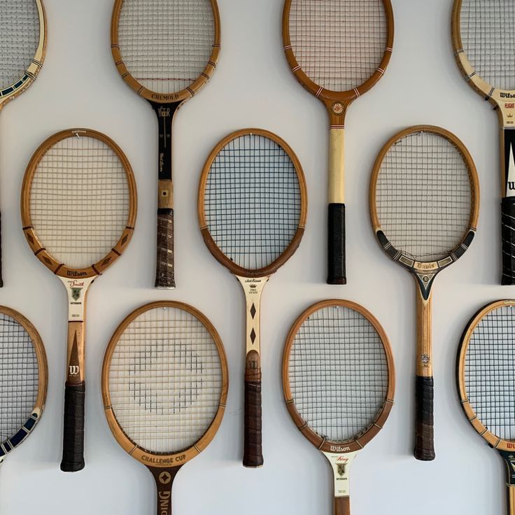 tennis rackets lined up in rows against a white wall with black and gold trim