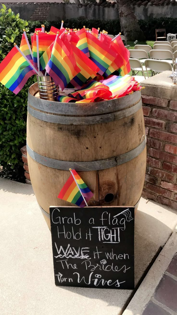 a wooden barrel filled with rainbow flags and a sign that says grab a flag hold in tight