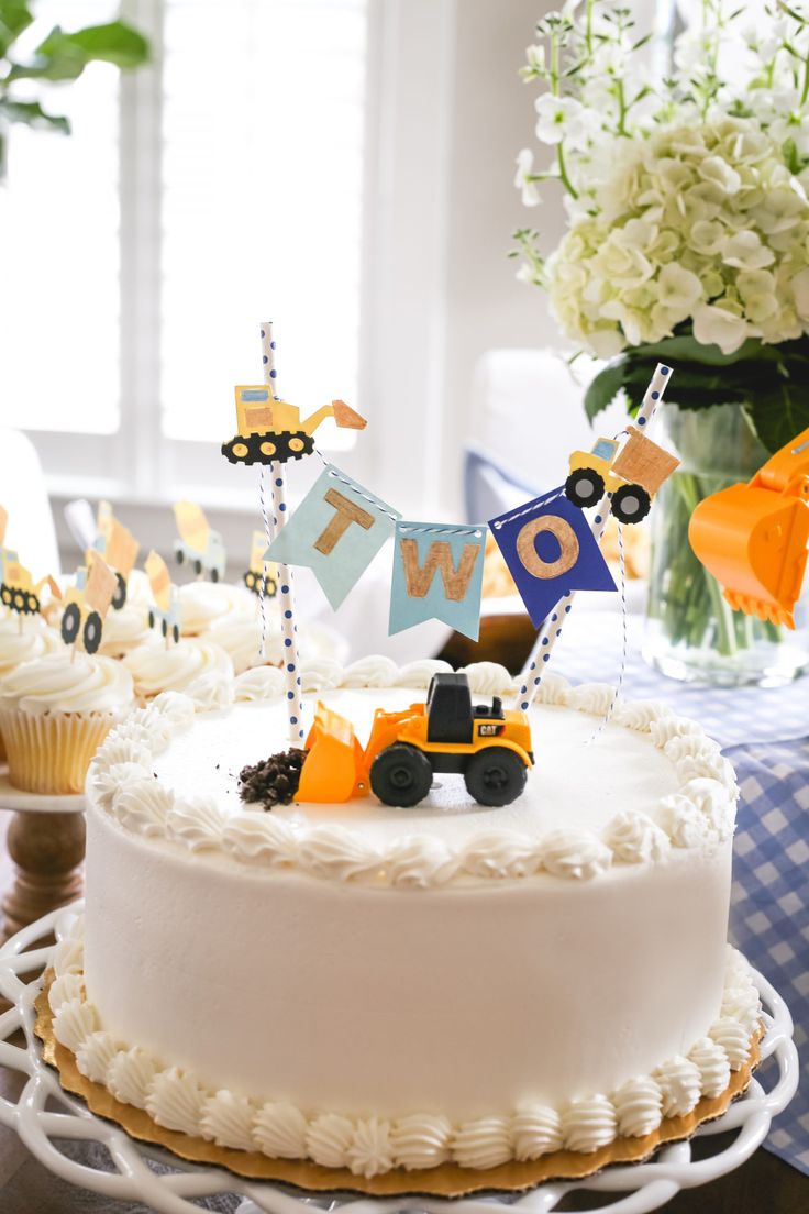 a birthday cake on a table with cupcakes in the shape of trucks and cars