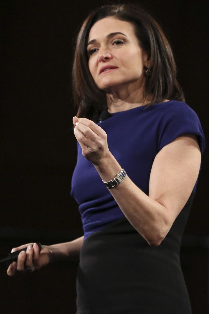 a woman standing in front of a black background with her hands together and looking off to the side