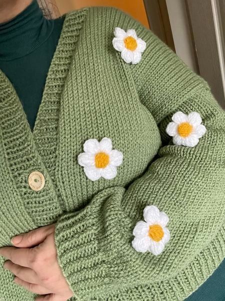 a woman wearing a green cardigan with white flowers on the front and yellow centers