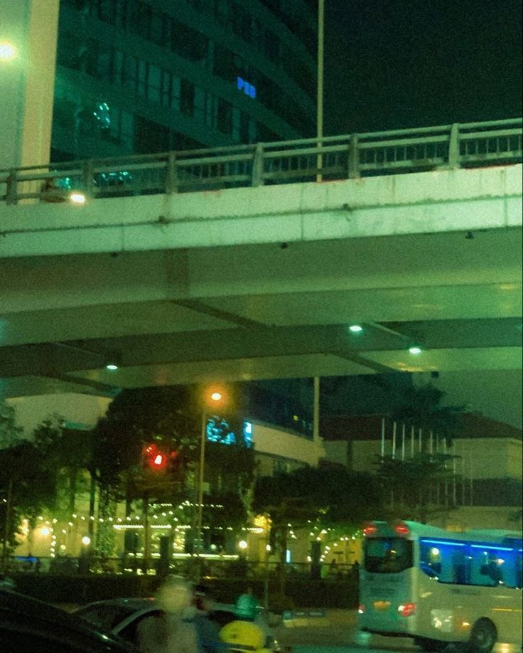 a city street at night with cars, buses and people on the sidewalk under an overpass