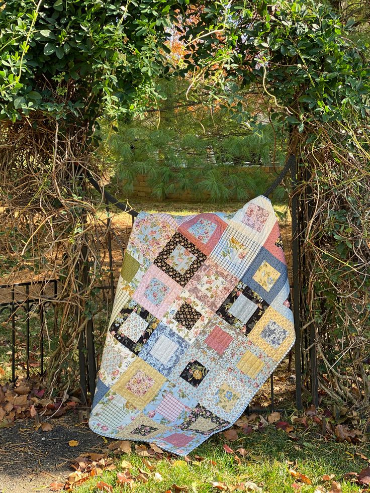 a patchwork quilt hanging on a fence in the fall time with leaves around it