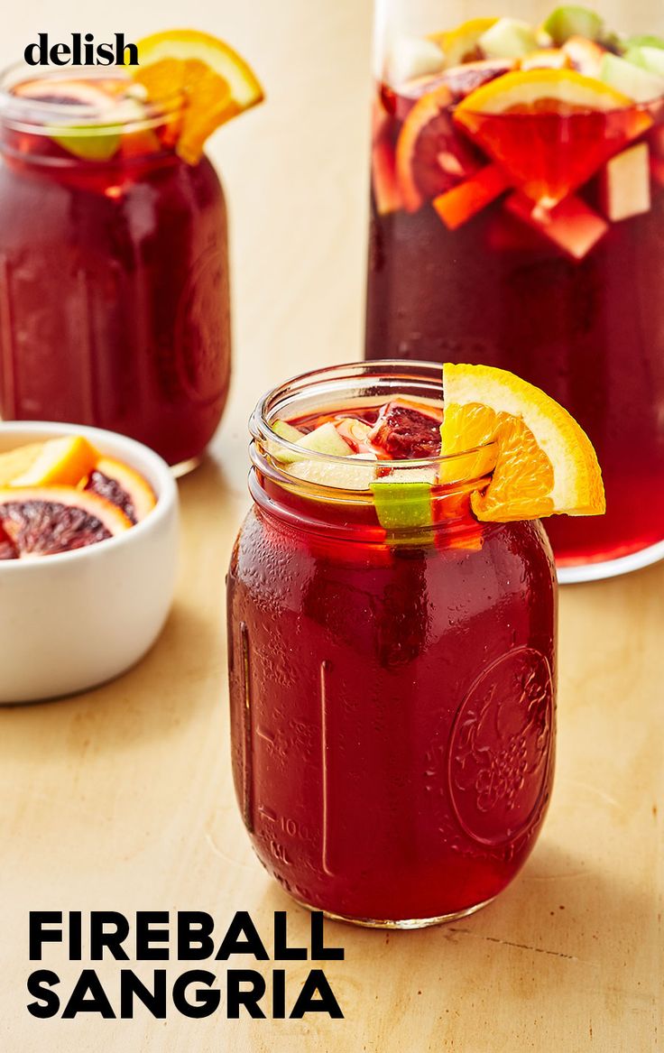 two mason jars filled with fruit and garnish on top of a wooden table