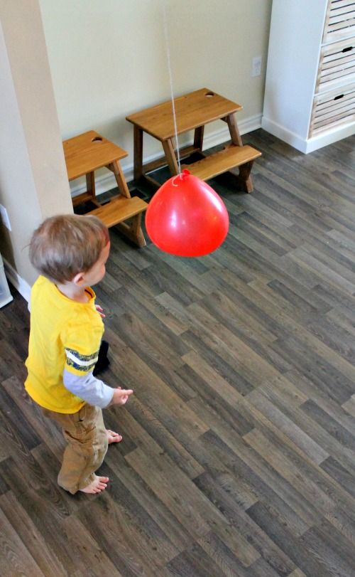 a young boy standing on top of a wooden floor next to a red ballon