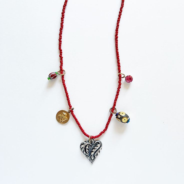 This one-of-a-kind necklace features a mix of new and vintage elements including glass and glitter beads combined with a Swarovski crystal, a solid brass Mercury charm, silver plated heart charm hanging from a strand of red colored glass seed beads on waxed poly/cotton cord. About 26" long. Handmade in the USA. Please note: This collage necklace is a one-of-a-kind, unique piece and it is FINAL SALE so please email with any questions or concerns before purchasing. Red Heart-shaped Beaded Necklaces, Heart-shaped Beaded Festive Jewelry, Heart Shaped Beaded Jewelry For Festive Occasion, Festive Beaded Heart Jewelry, Festive Heart-shaped Beaded Jewelry, Red Heart Beads Necklace With Heart Pendant, Red Heart-shaped Beaded Necklace, Handmade Red Bohemian Charm Necklaces, Bohemian Beaded Necklaces With Heart Charm