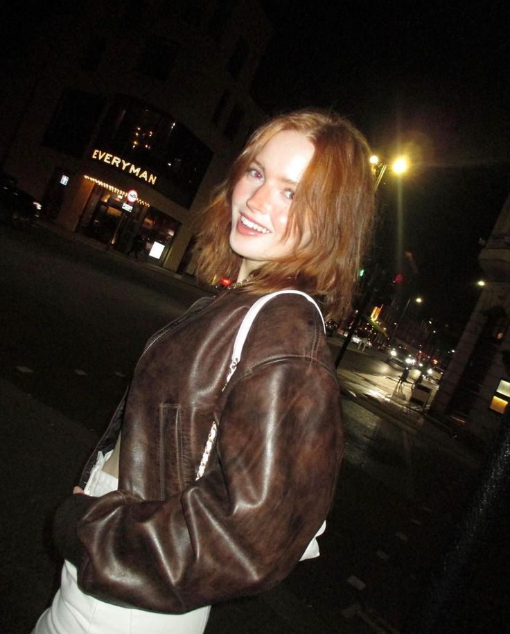 a woman standing in the street at night with her hand on her hip and smiling