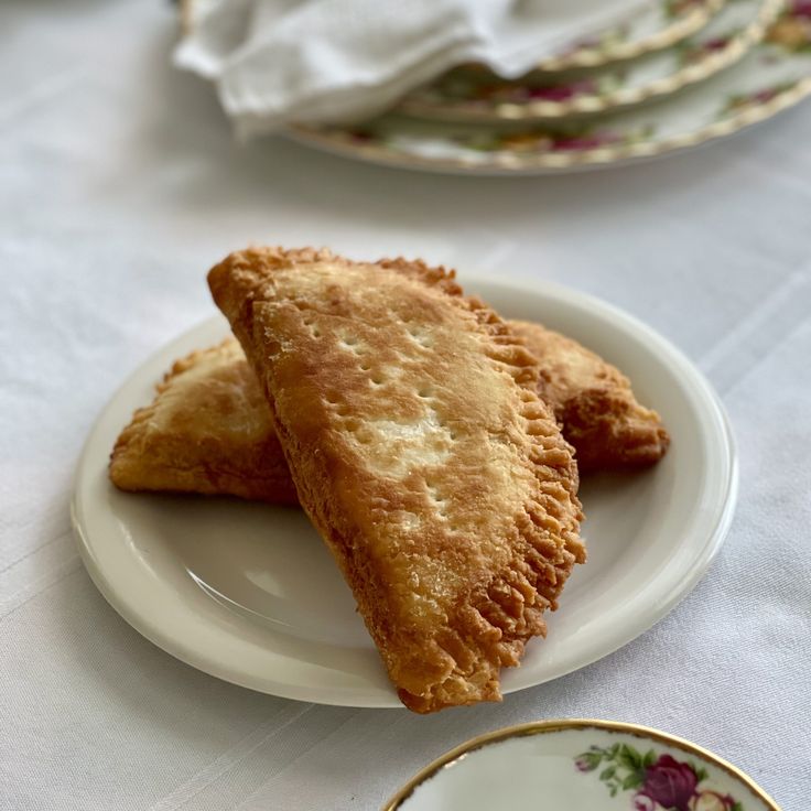 two pastries on a white plate next to a cup and saucer with flowers