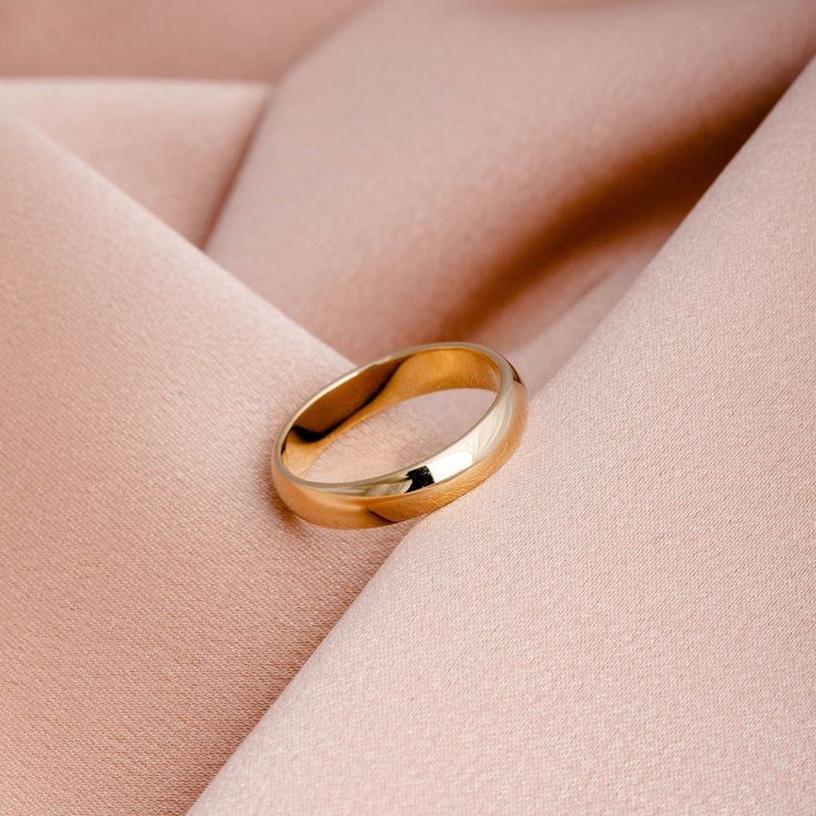 a gold wedding ring sitting on top of a pink fabric