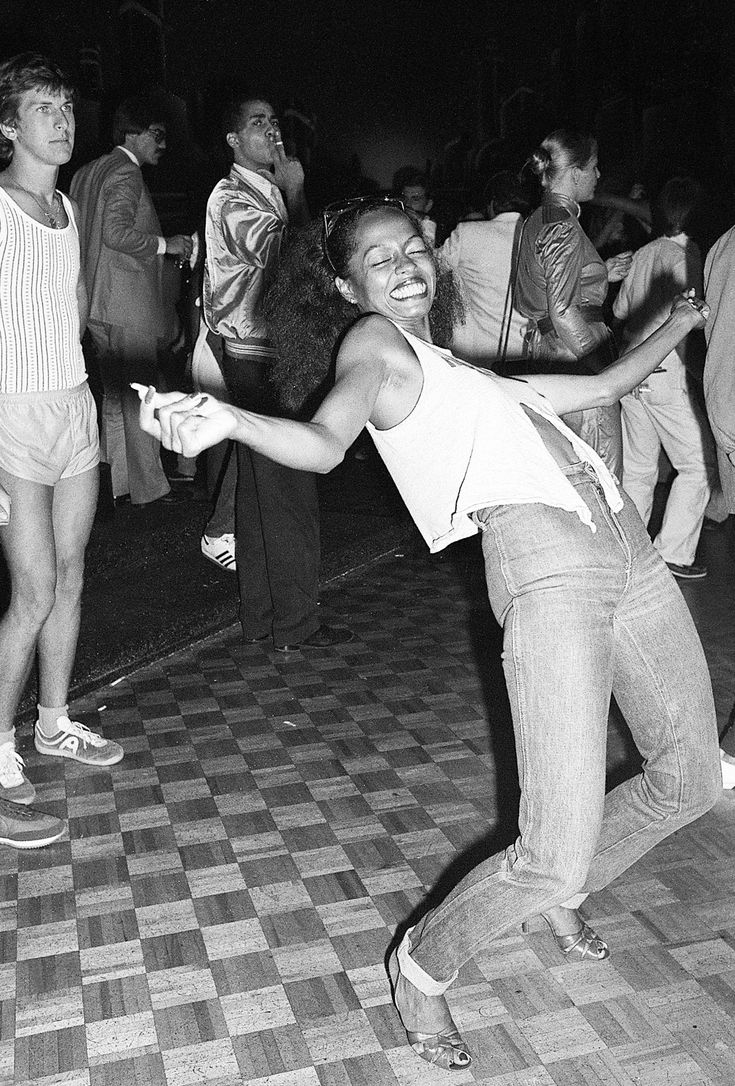 a black and white photo of a woman dancing on the dance floor with people in the background