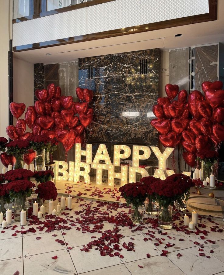 red flowers and candles are on the floor in front of a happy birthday sign with roses