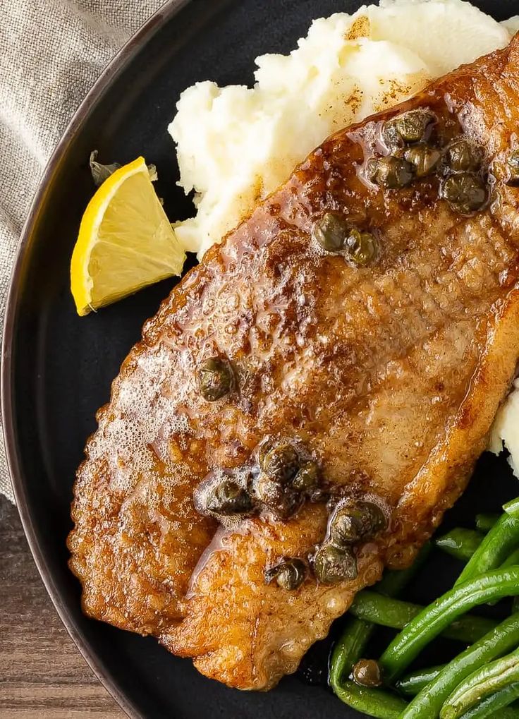 a black plate topped with meat, mashed potatoes and green beans