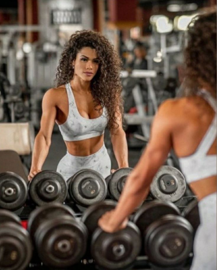 a woman standing in front of a pile of dumbs with another person behind her