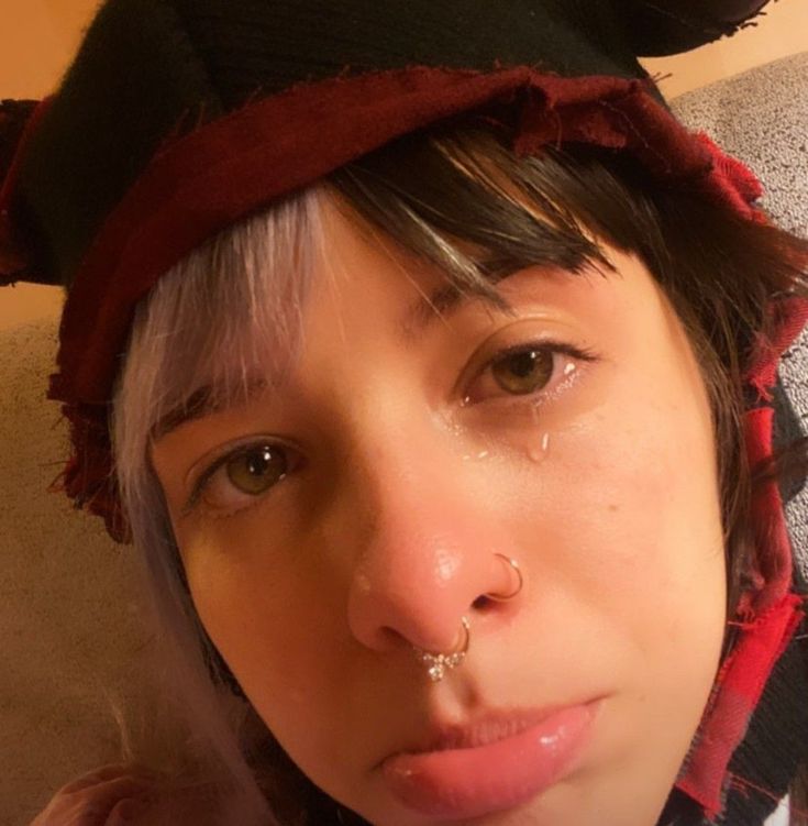 a woman with piercings on her nose wearing a red and black hat is looking at the camera