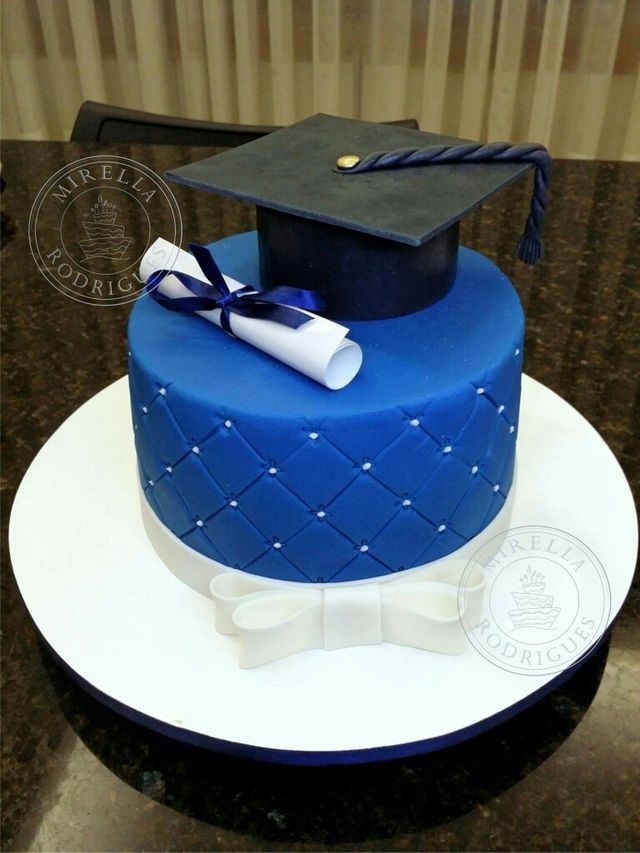 a blue graduation cake with a mortar and tassel on top, sitting on a table