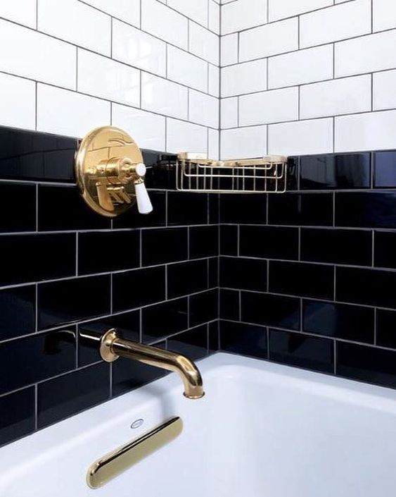 a black and white tiled bathroom with gold faucet, soap dispenser and bathtub